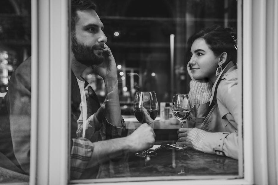 A couple enjoys a romantic evening with wine at a cozy cafe, captured through the window.