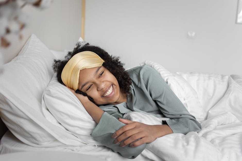 A joyful woman relaxing in a cozy bedroom, wearing a satin sleep mask and smiling brightly.