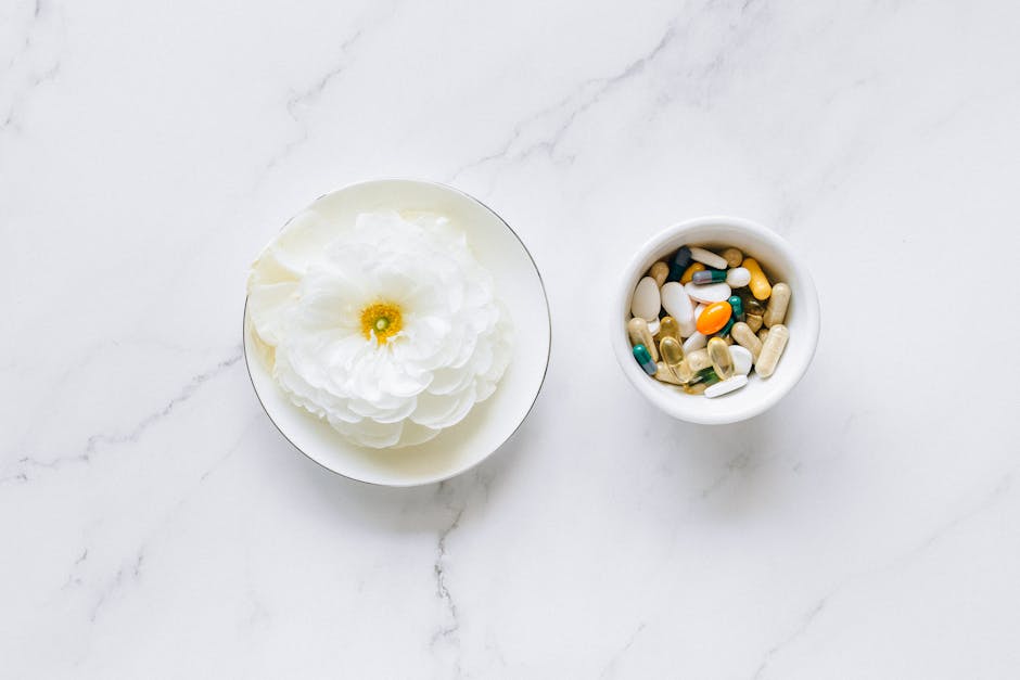 Flat lay of a white flower next to mixing pills on a marble surface, symbolizing natural vs synthetic remedies.