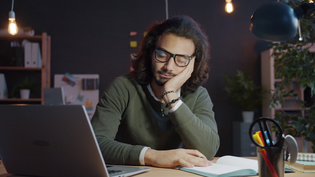 Man sleeping at desk with laptop and notebook.