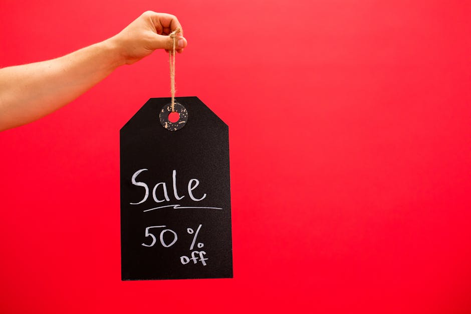 Hand holding a black sale tag with 50% off on a vibrant red background.