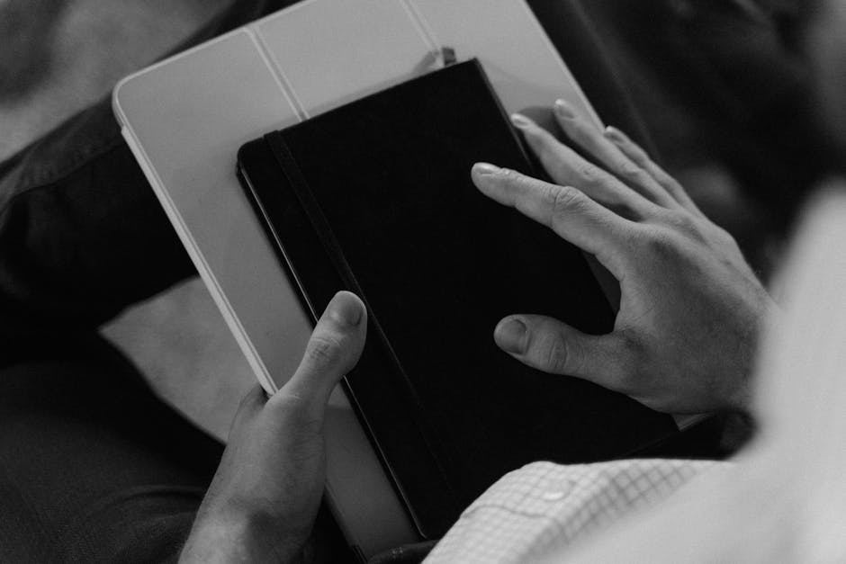 Black and white image of hands holding a book and tablet, depicting focus and calmness.