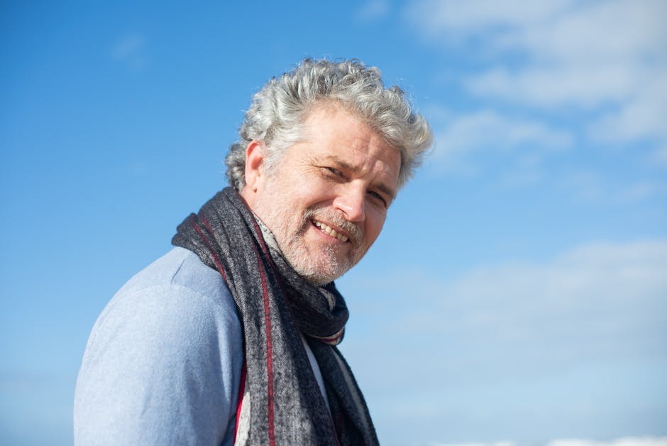Portrait of a smiling senior man wearing a scarf against a blue sky, conveying warmth and cheerfulness.