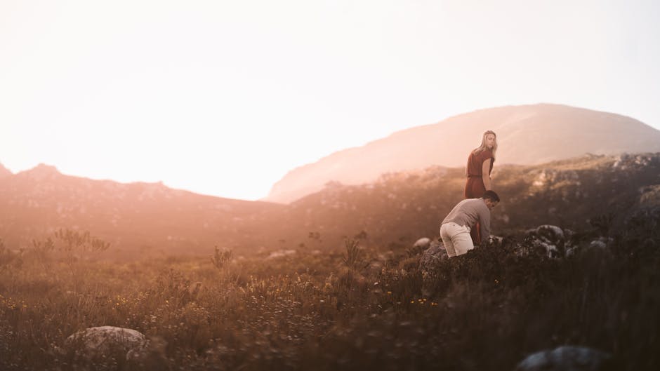 A couple stands in a misty mountain field at sunrise, embracing adventure.