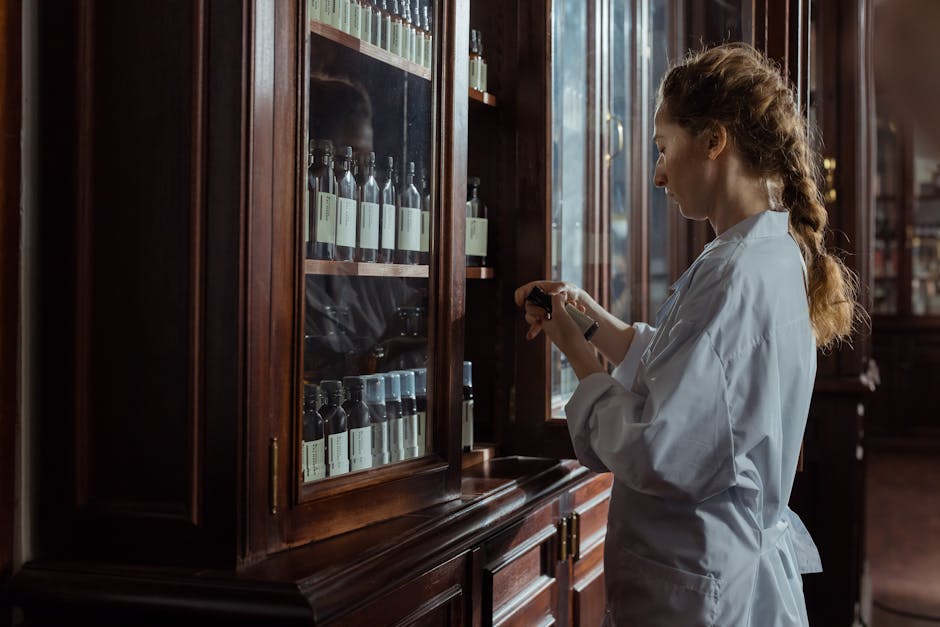 A female pharmacist in a white uniform organizing bottles in a pharmacy cabinet.