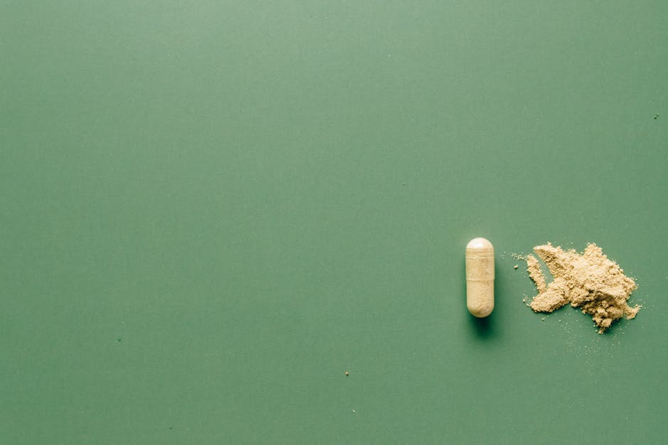 Close-up of herbal supplement capsule and powder on a minimalist green surface.