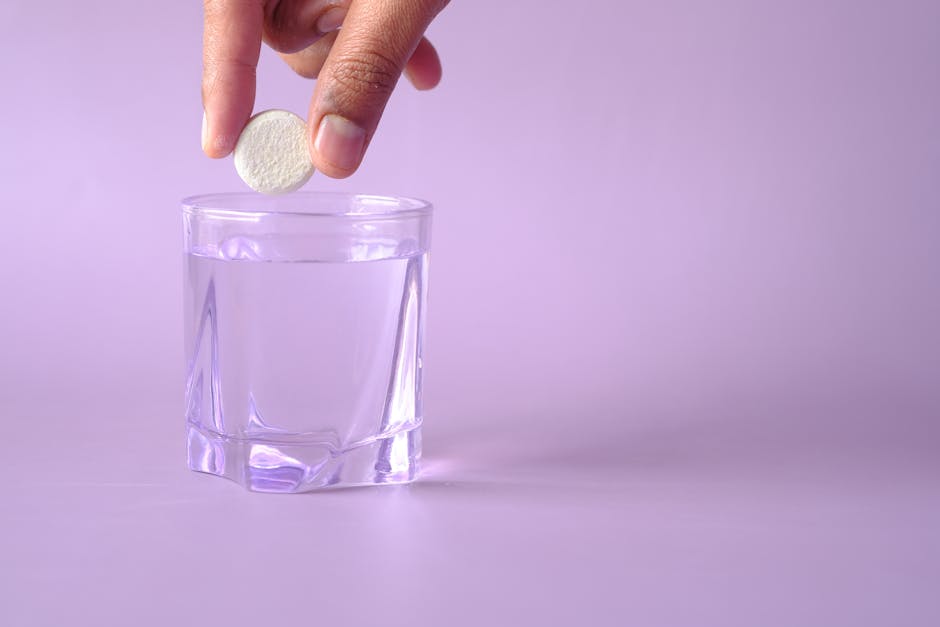 Close-up of a tablet being dropped into a glass of water on a purple background, creating bubbles.