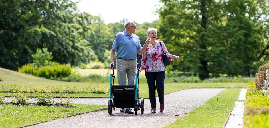 Senior couple walking in a park with a walker, enjoying a sunny day outdoors.