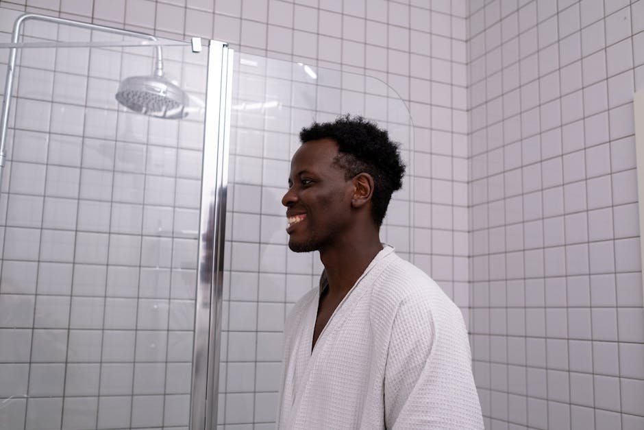 African American man smiling in bathrobe inside tiled bathroom. Bright and candid setting.