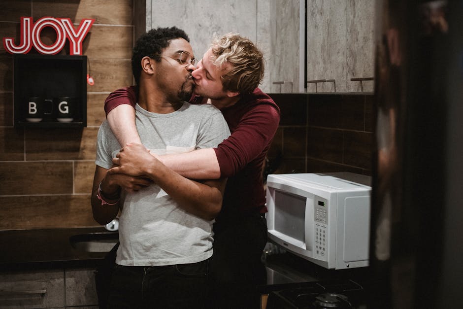 A loving interracial gay couple shares a kiss in their cozy kitchen, embracing affection and joy.