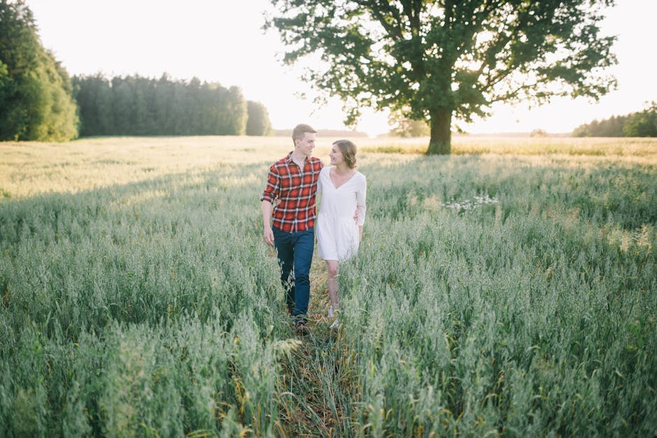 A couple walks hand in hand through a serene wheat field during sunset.