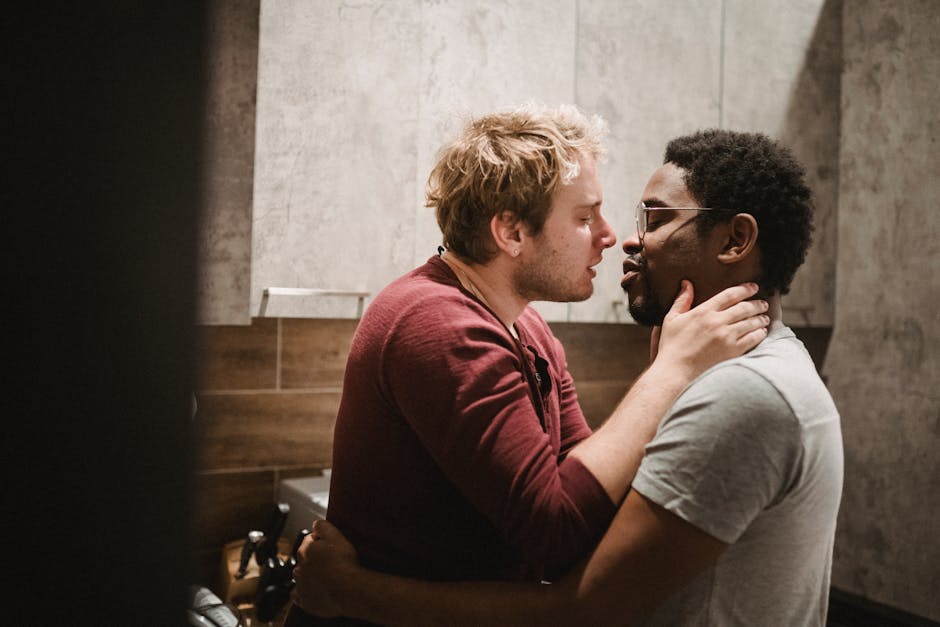 A loving interracial LGBTQ couple embraces tenderly in a cozy indoor setting.